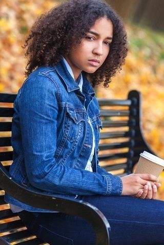 A young woman is sitting on a park bench holding a cup of coffee.