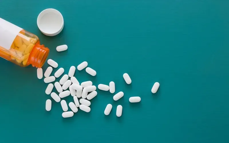 A bottle of pills is pouring out of it on a blue surface.