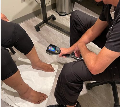 A person sitting in a chair receiving a nerve scan on their feet by a doctor