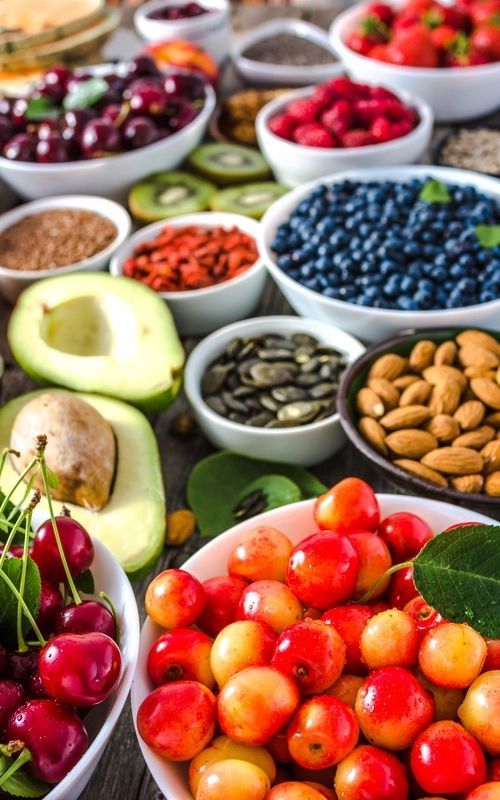 A variety of fruits and vegetables in bowls on a table.