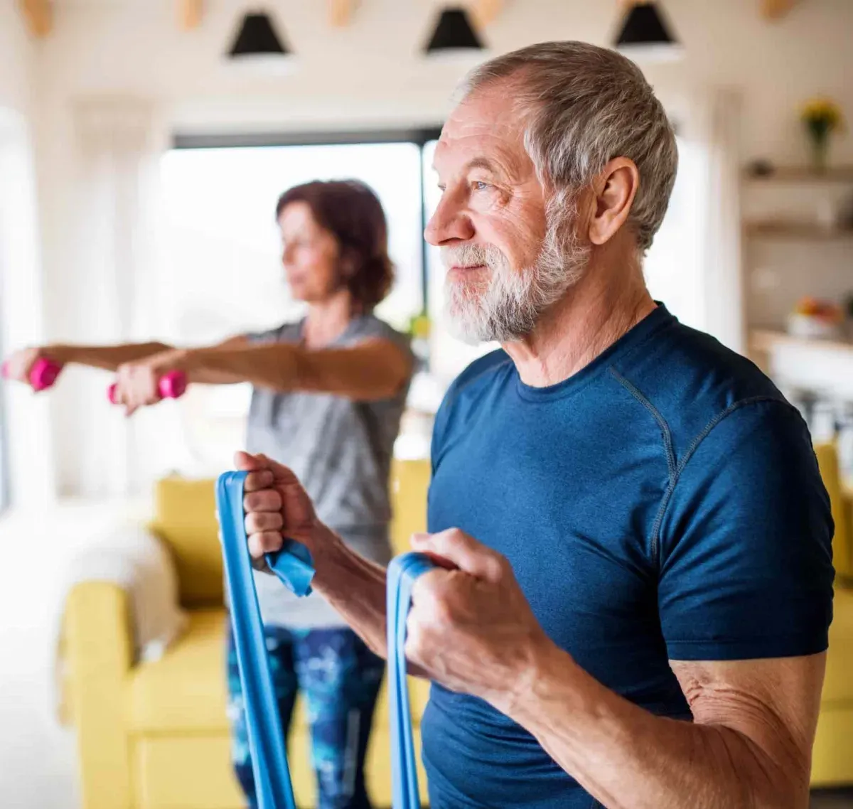 A man and a woman are doing exercises with resistance bands in a living room.