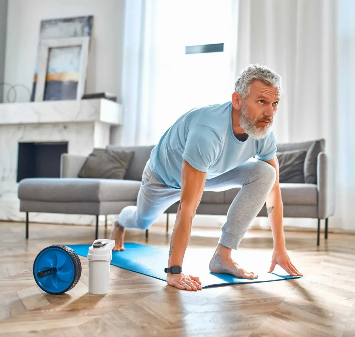 A man is kneeling on a yoga mat in a living room.