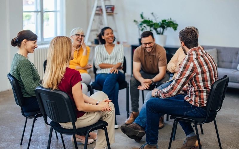 A group of people are sitting in a circle in chairs having a conversation.