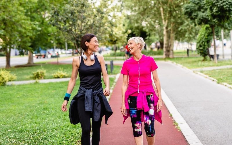 Two women are walking down a path in a park holding hands.