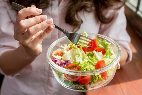 A woman is eating a salad with a fork from a glass bowl.