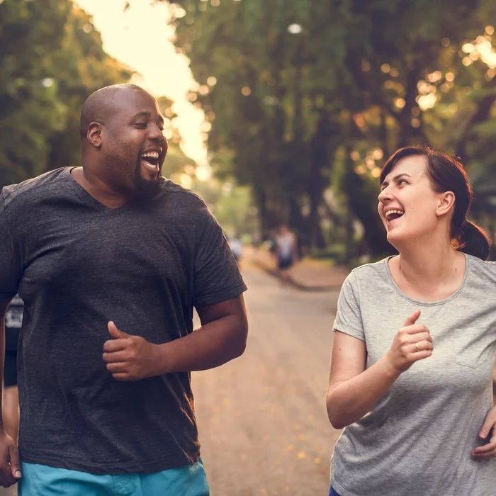 A man and a woman are laughing while running down a street