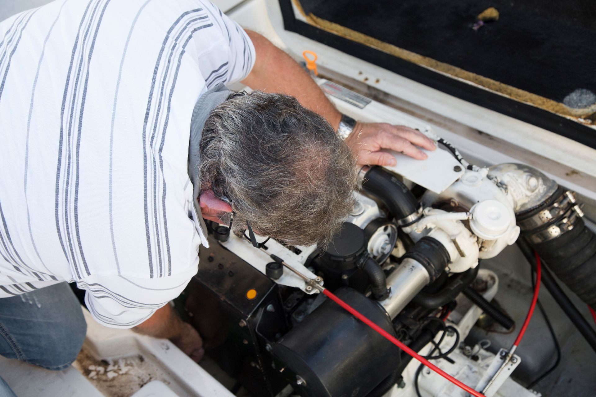 Un technicien inspecte le compartiment moteur d'un bateau, où les câbles et les tuyaux sont apparents.