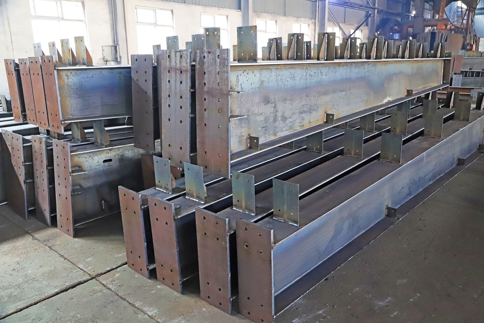 De grandes poutres métalliques et des composants en acier soudé empilés dans un atelier industriel