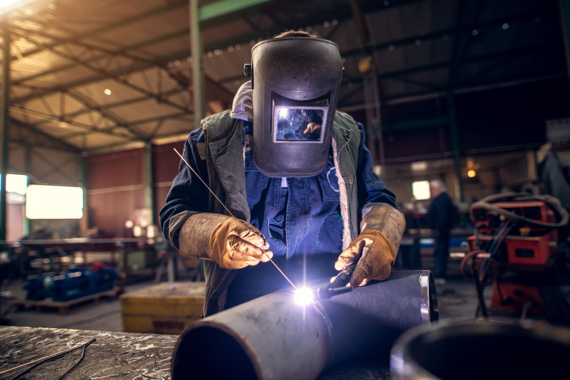 Soudeur en tenue de protection soude un tuyau métallique dans un atelier d'usine ; des étincelles jaillissent.