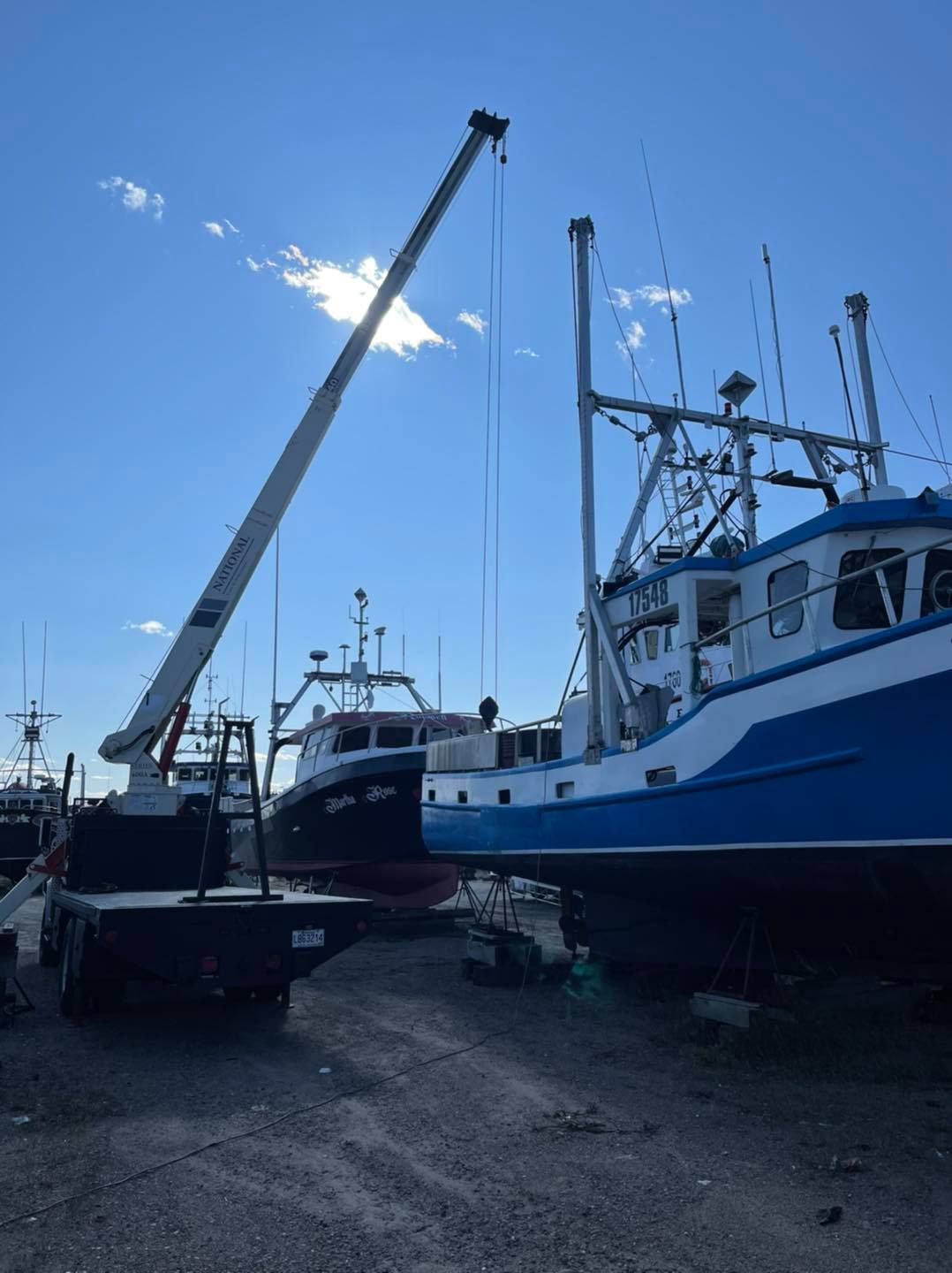 Des bateaux de pêche amarrés dans un port, dont un grand bateau bleu et blanc sous un ciel d'un bleu limpide.