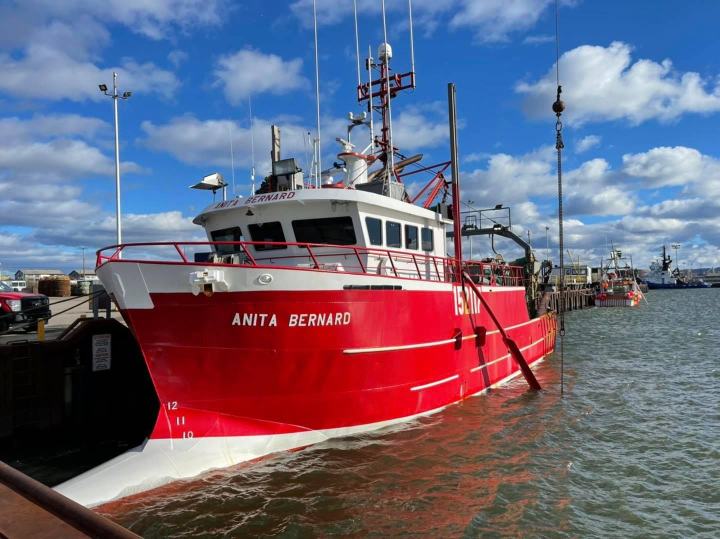 Un bateau de pêche rouge nommé ANTI BEWARD était amarré dans un port sous un ciel nuageux.