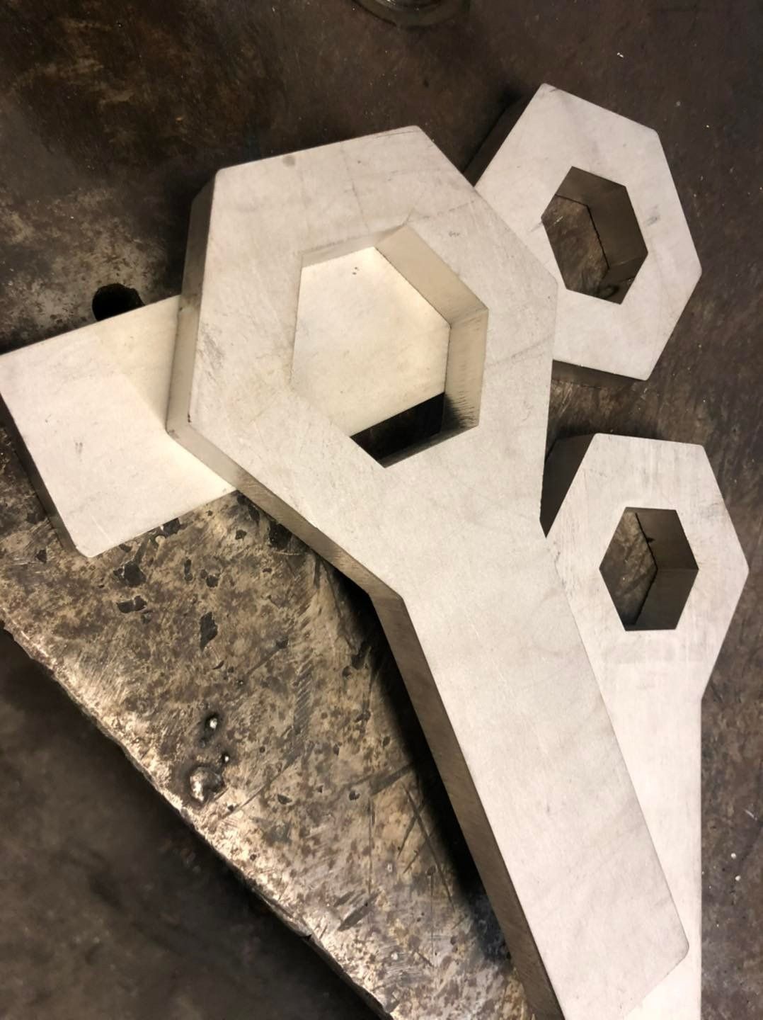 Découpes géométriques en métal blanc avec des trous hexagonaux empilées sur un sol en béton brut