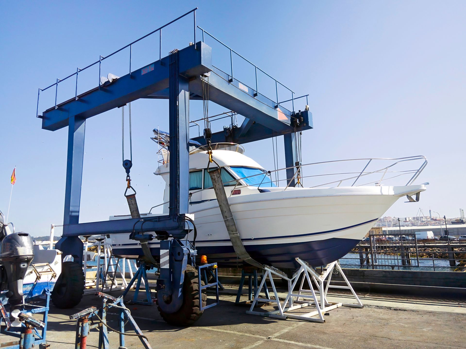 Bateau sur un élévateur dans un chantier naval, avec une grande grue bleue et des équipements de quai à proximité.