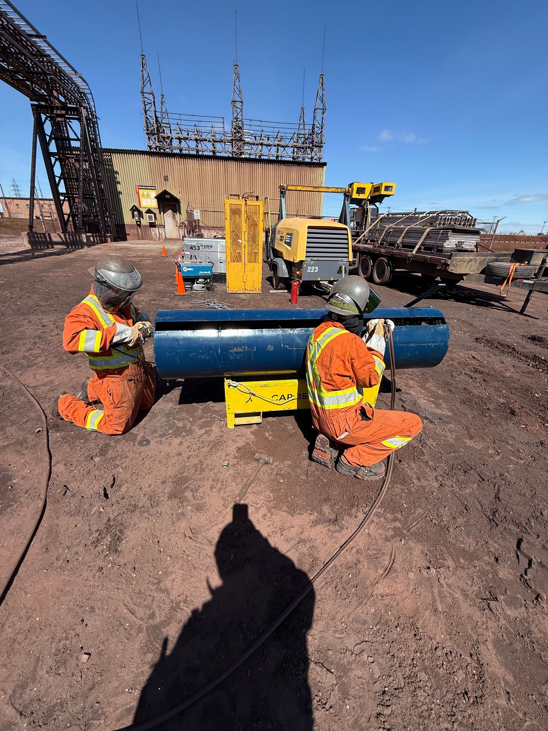 Des ouvriers en tenue de sécurité orange manipulent un gros tuyau bleu sur un chantier de construction.