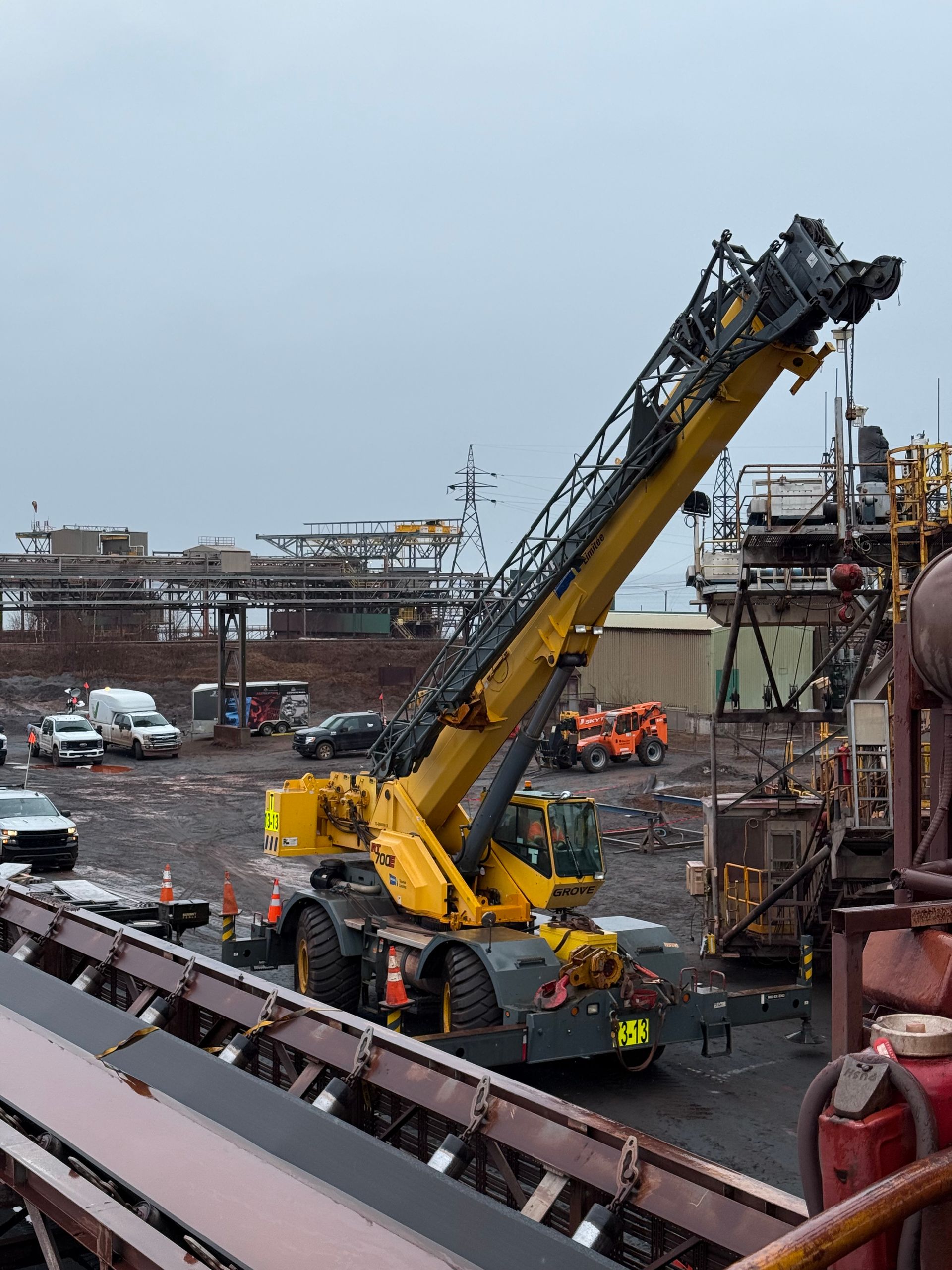 Une grue jaune effectue des levages dans un chantier naval animé, à côté d'un navire à quai, avec des ouvriers et du matériel à proximité.