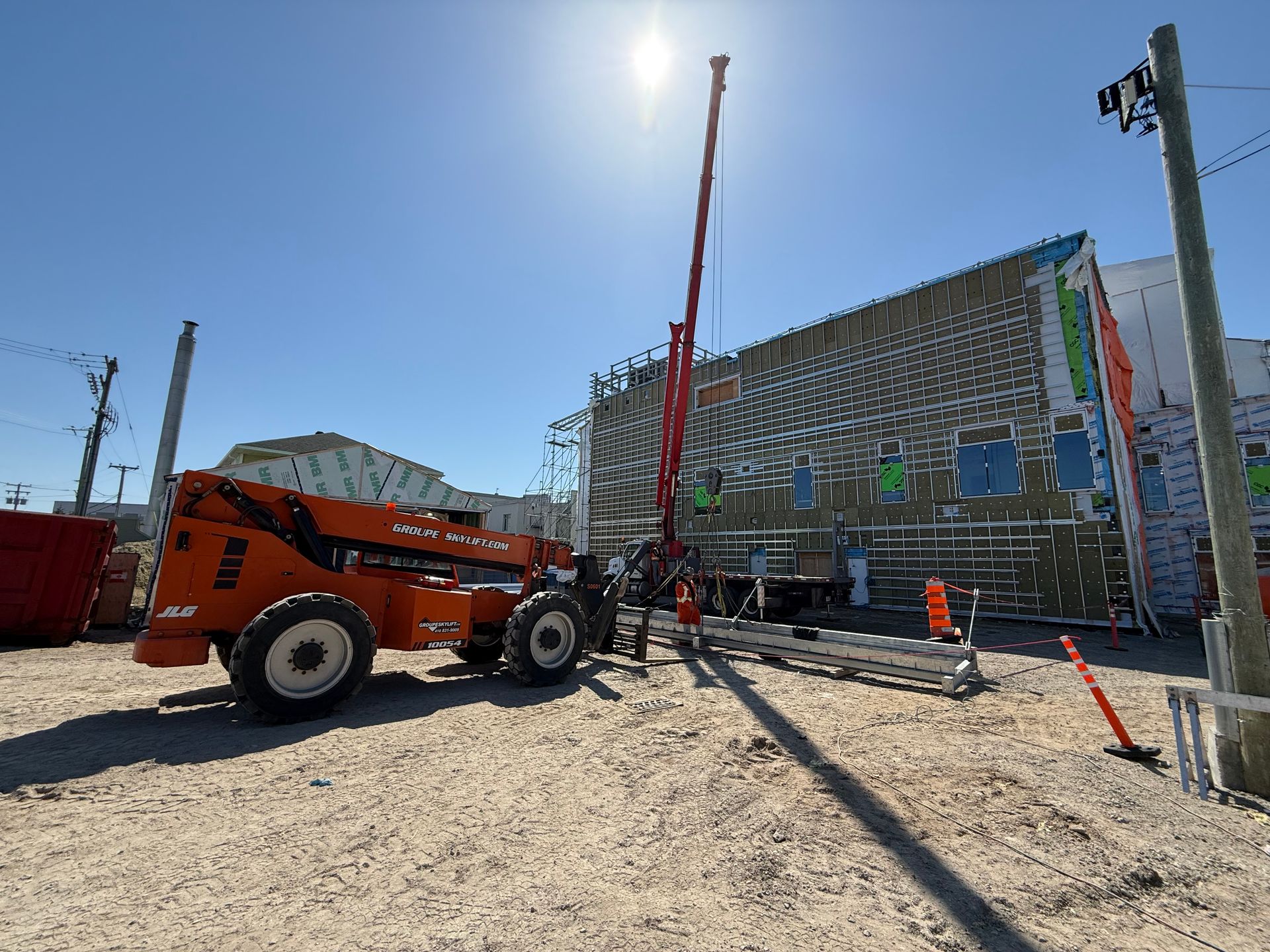 Chantier de construction avec nacelle élévatrice orange à côté d'un bâtiment en réparation, journée ensoleillée.