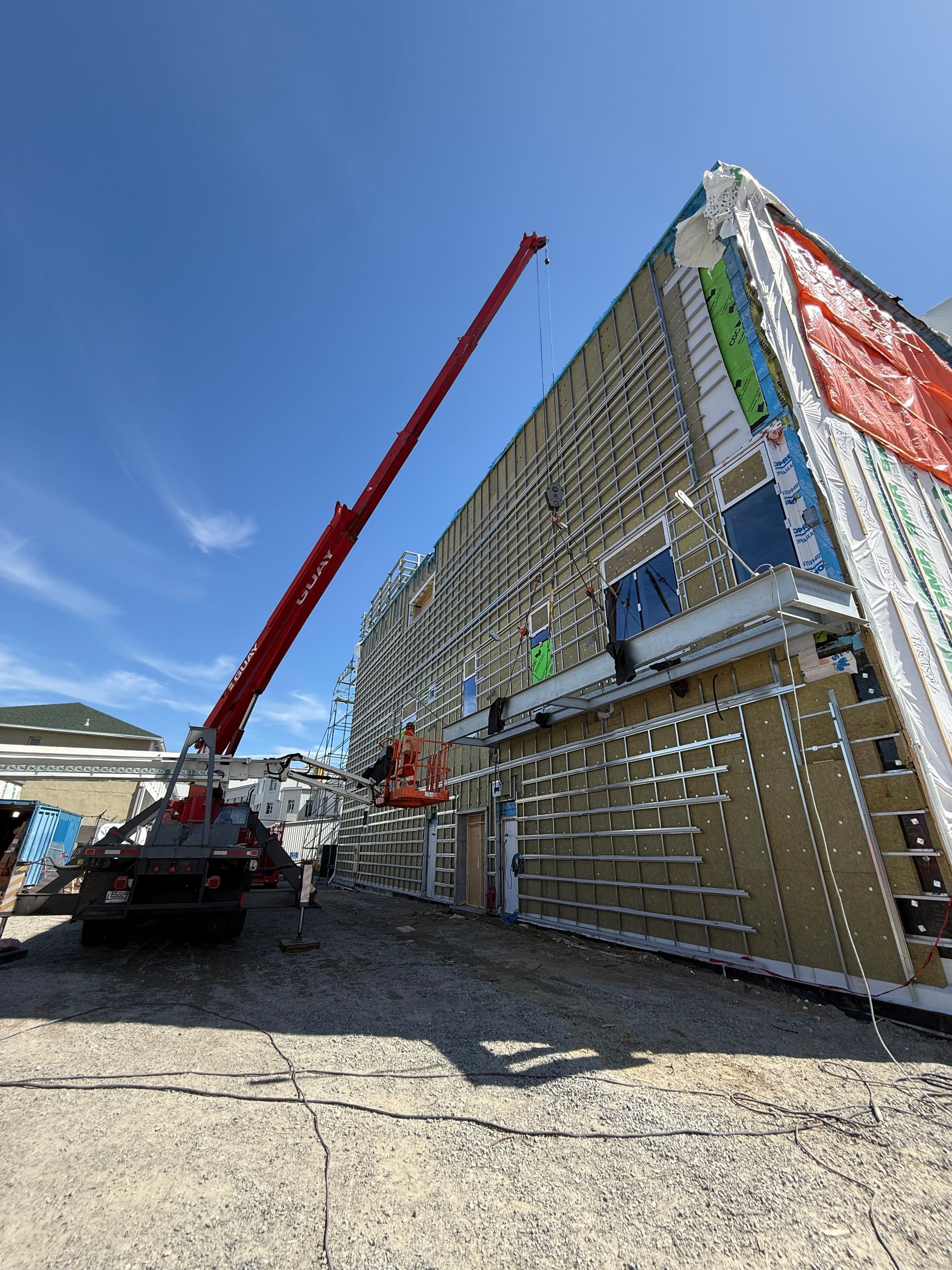 Chantier de construction avec une grue rouge soulevant des matériaux à côté d'un grand bâtiment en construction