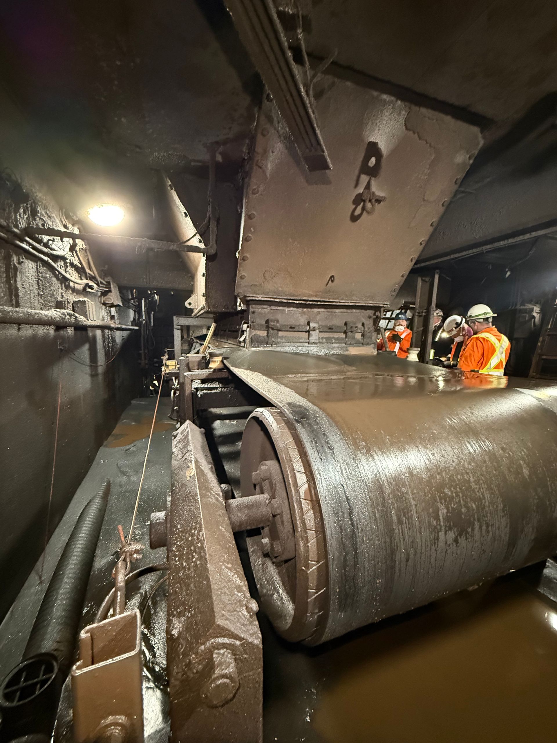 Travaux d'entretien de canalisations industrielles dans un tunnel inondé : des ouvriers en tenue de sécurité orange inspectent une grosse canalisation métallique.