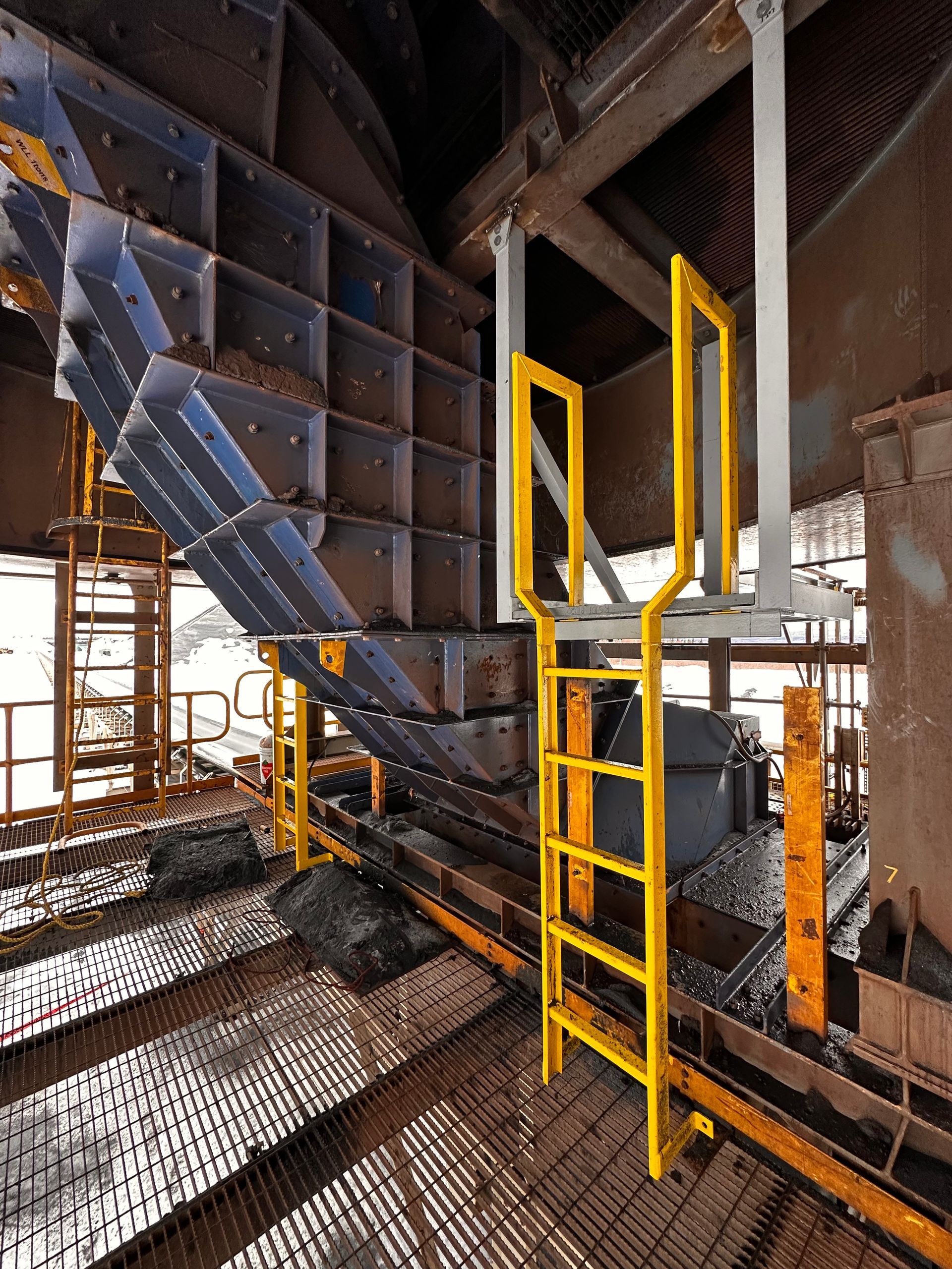 Échelle de sécurité jaune sur une structure métallique industrielle à l'intérieur d'une aciérie.
