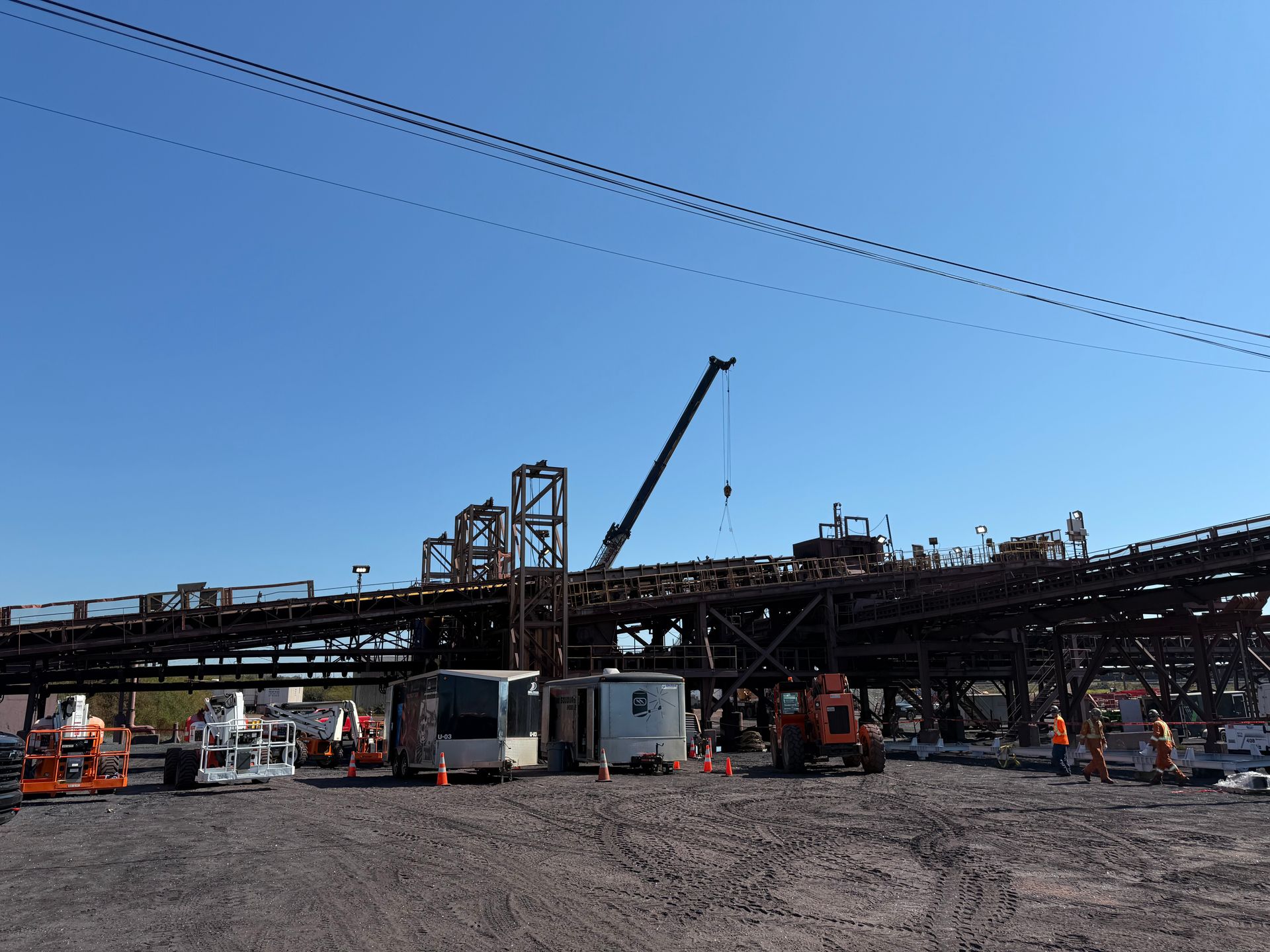 Usine industrielle avec ouvriers, grues et machines sous un ciel bleu clair