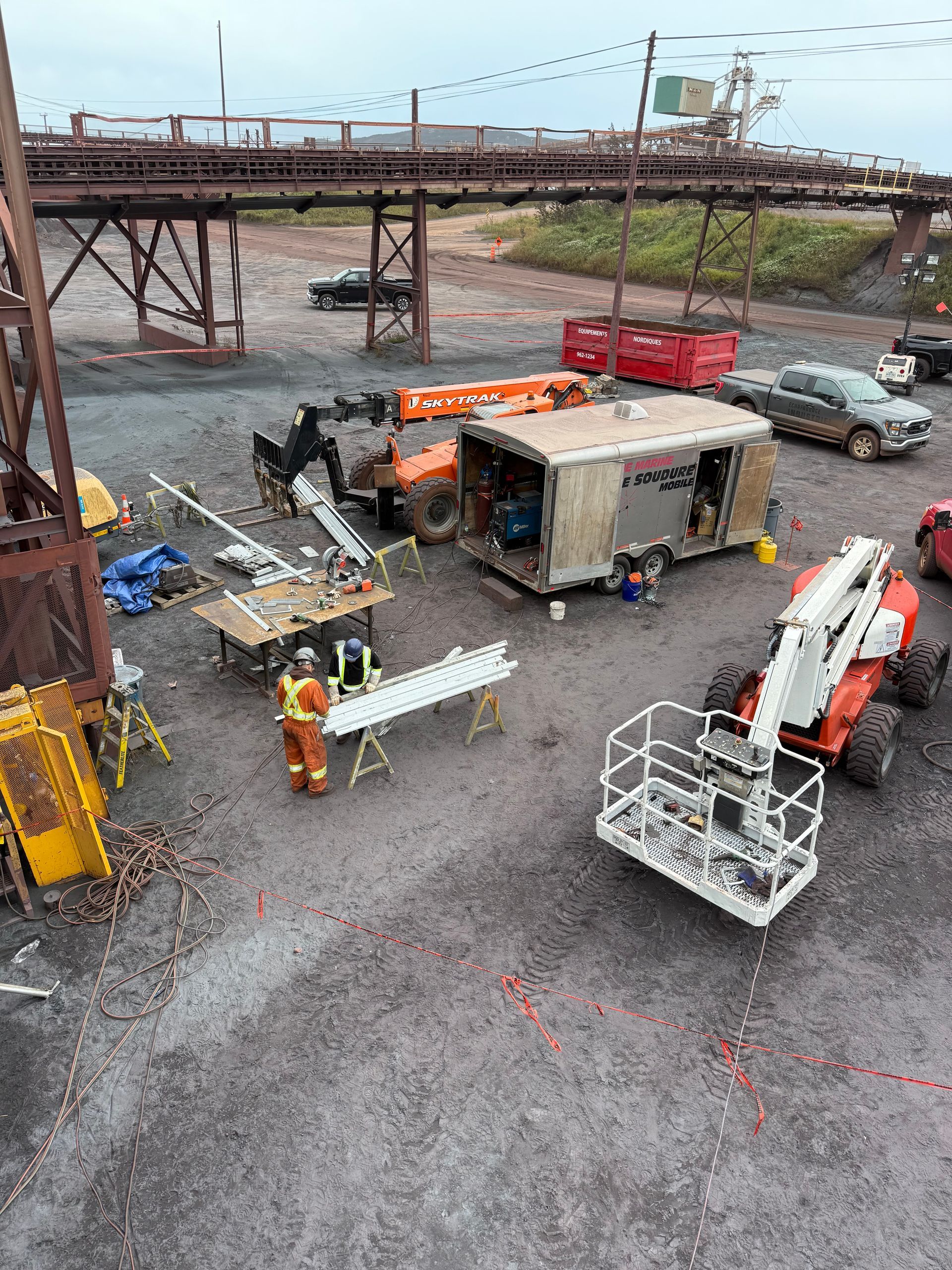 Chantier de construction avec camions utilitaires, grue, ouvriers et équipements près d'une structure de pont métallique