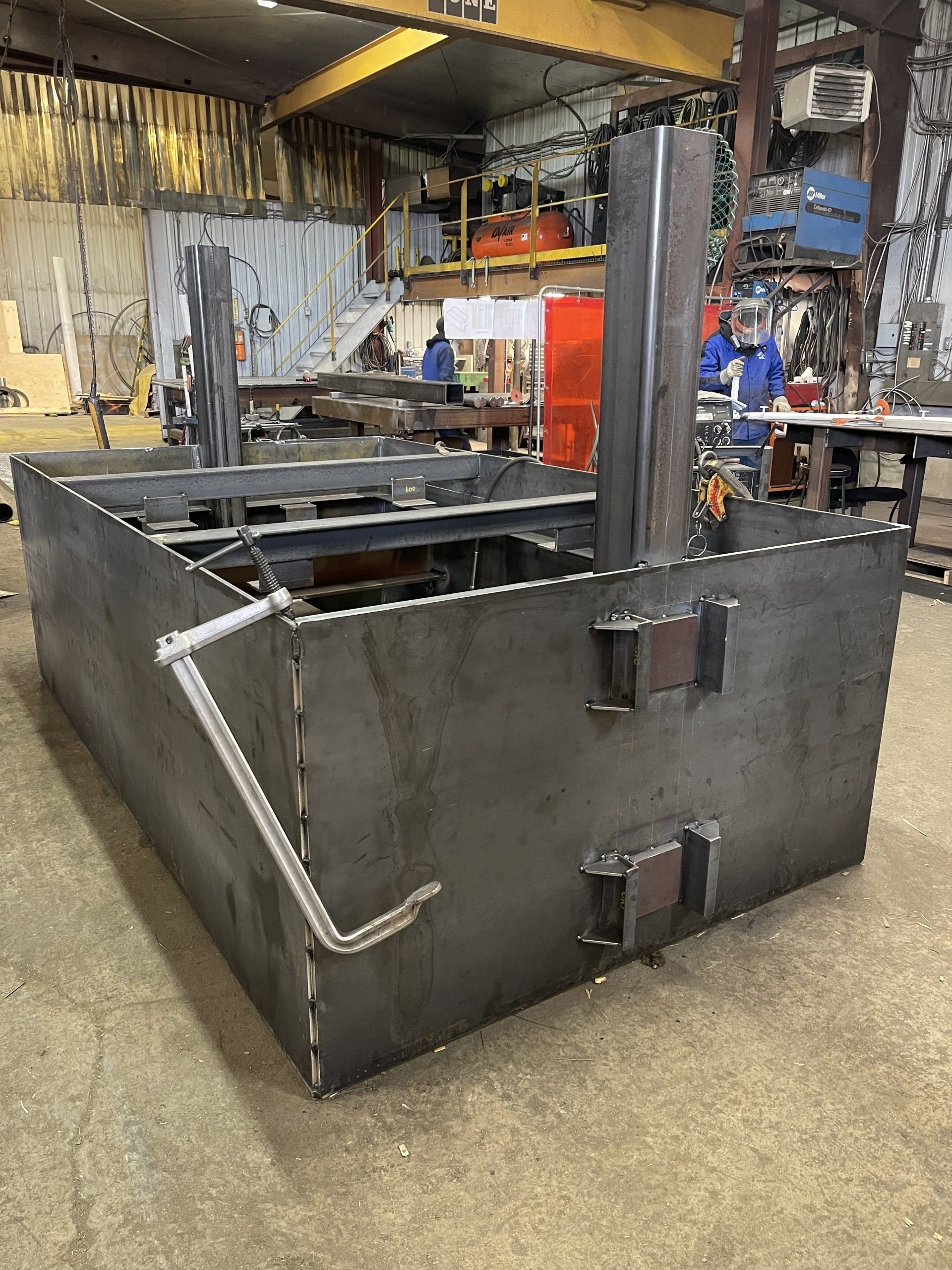 Grande structure métallique noire dans un atelier industriel, avec dessus ouvert et portes renforcées.