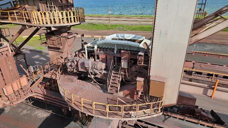 Machines industrielles rouillées dans une usine en bord de mer, avec des rambardes et l'océan en arrière-plan.
