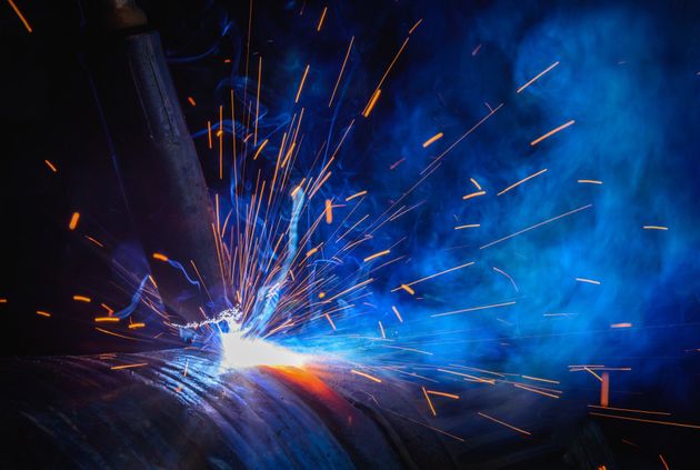 Des étincelles de soudure éclatent dans un décor industriel bleu foncé.