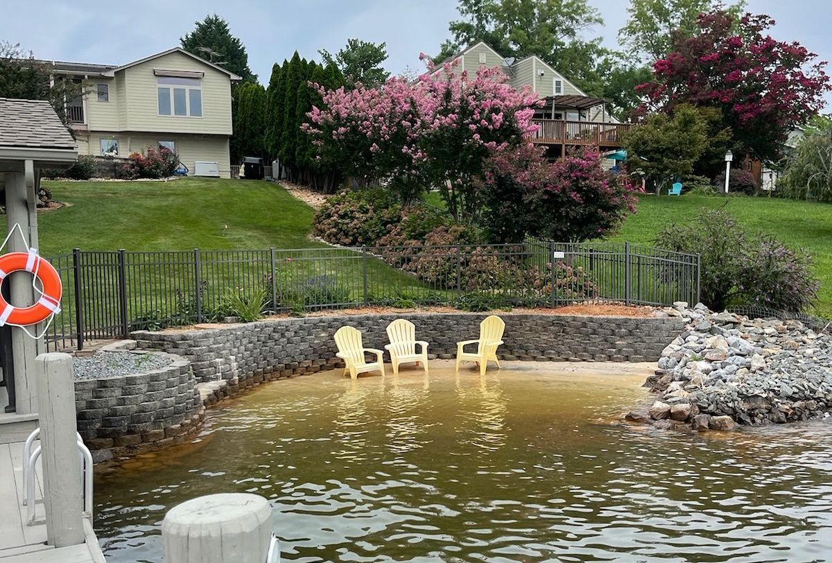 Lakeside seating area with yellow chairs, surrounded by a stone wall, water, and trees.