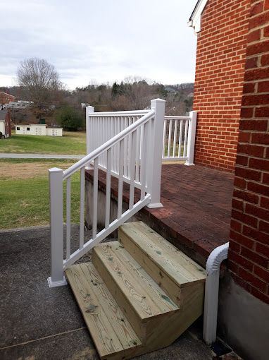 Wooden steps leading up to a deck with white railings next to a brick building. Wooden steps leading up to a deck with white railings next to a brick building.