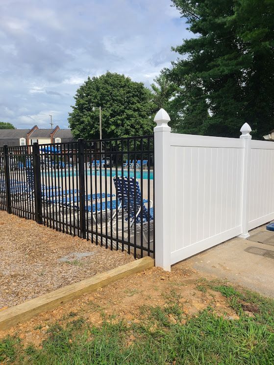Black metal and white vinyl fences surround a swimming pool area with blue chairs and cloudy sky.