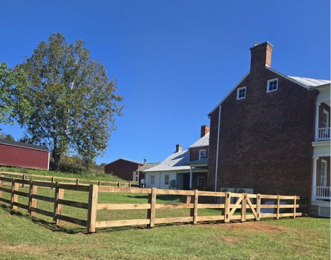 Wooden fence surrounds a grassy area with a brick building and gate under a blue sky.