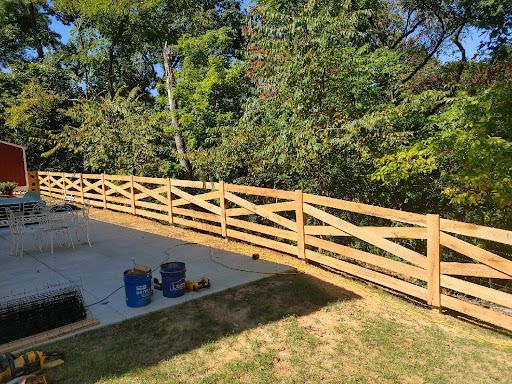 Wooden fence with crisscross design borders a yard, lush greenery in the background.