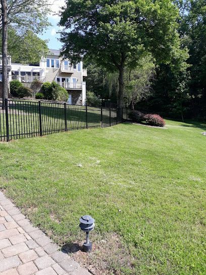 Lawn in front of a house, black fence, and trees. A solar-powered light is in the grass.
