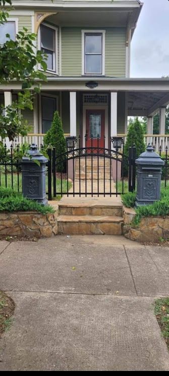 A two-story green house with a porch and a black metal gate leading to the front door.
