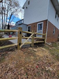 A split-rail fence with a gate surrounds a patio next to a two-story brick and white-sided house.