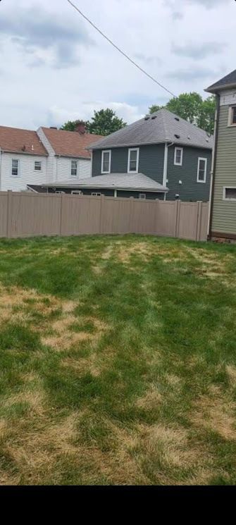 Backyard view of houses behind a brown fence and grass. A cloudy sky is overhead.
