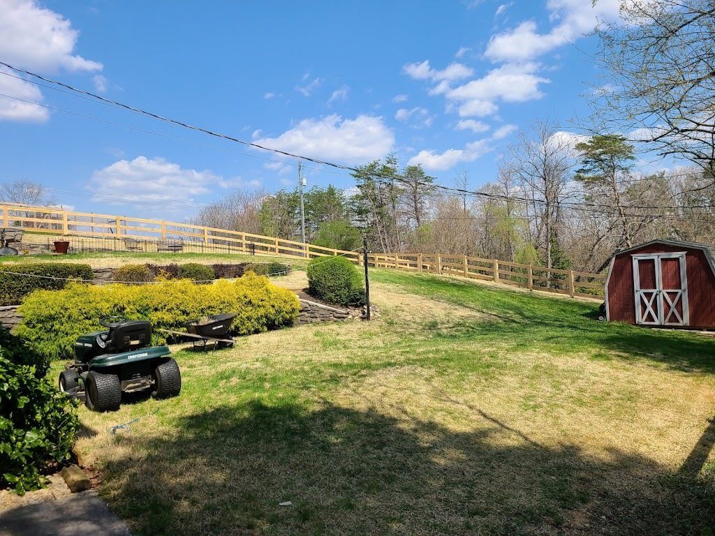A backyard scene with a riding lawnmower, shed, fence, and a blue sky with clouds.