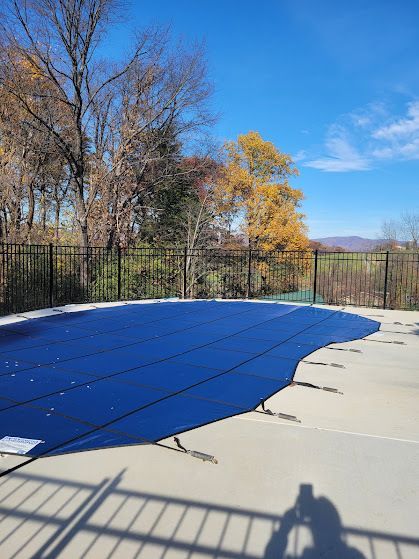 Blue pool cover on a concrete patio, black fence, trees with fall foliage, sunny day.