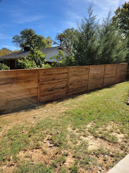 Wooden fence in a yard with grass and trees, under a blue sky.