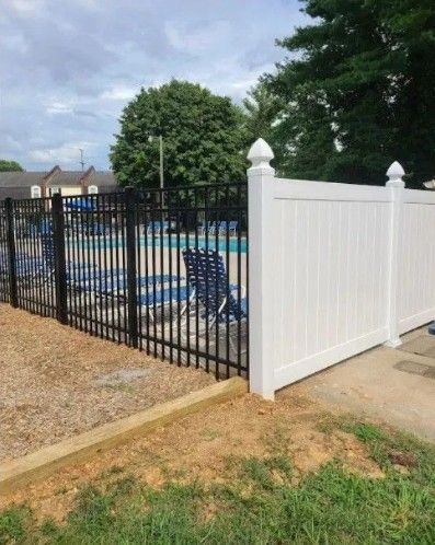 White picket fence with gate in a yard with grass and small rocks, trees in background. White picket fence with gate in a yard with grass and small rocks, trees in background.