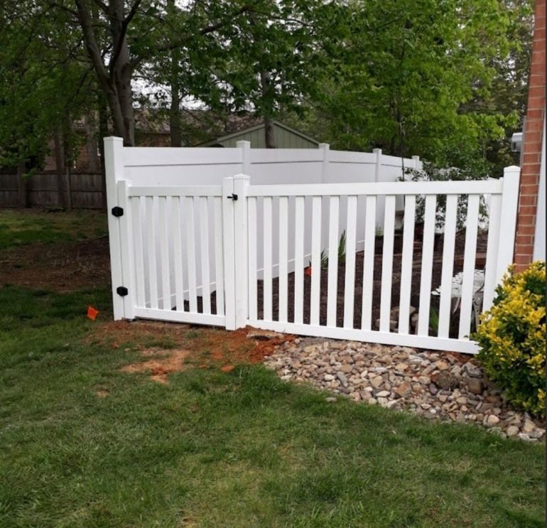 White vinyl fence with gate installed along a landscaped garden bed.
