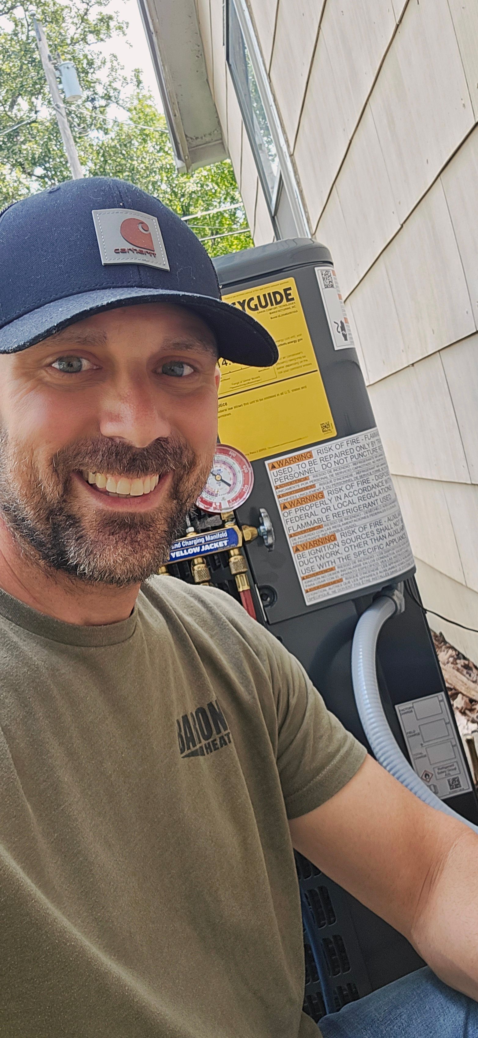 Technician servicing an outdoor HVAC unit with gauges beside a Barone’s Heat & Air logo