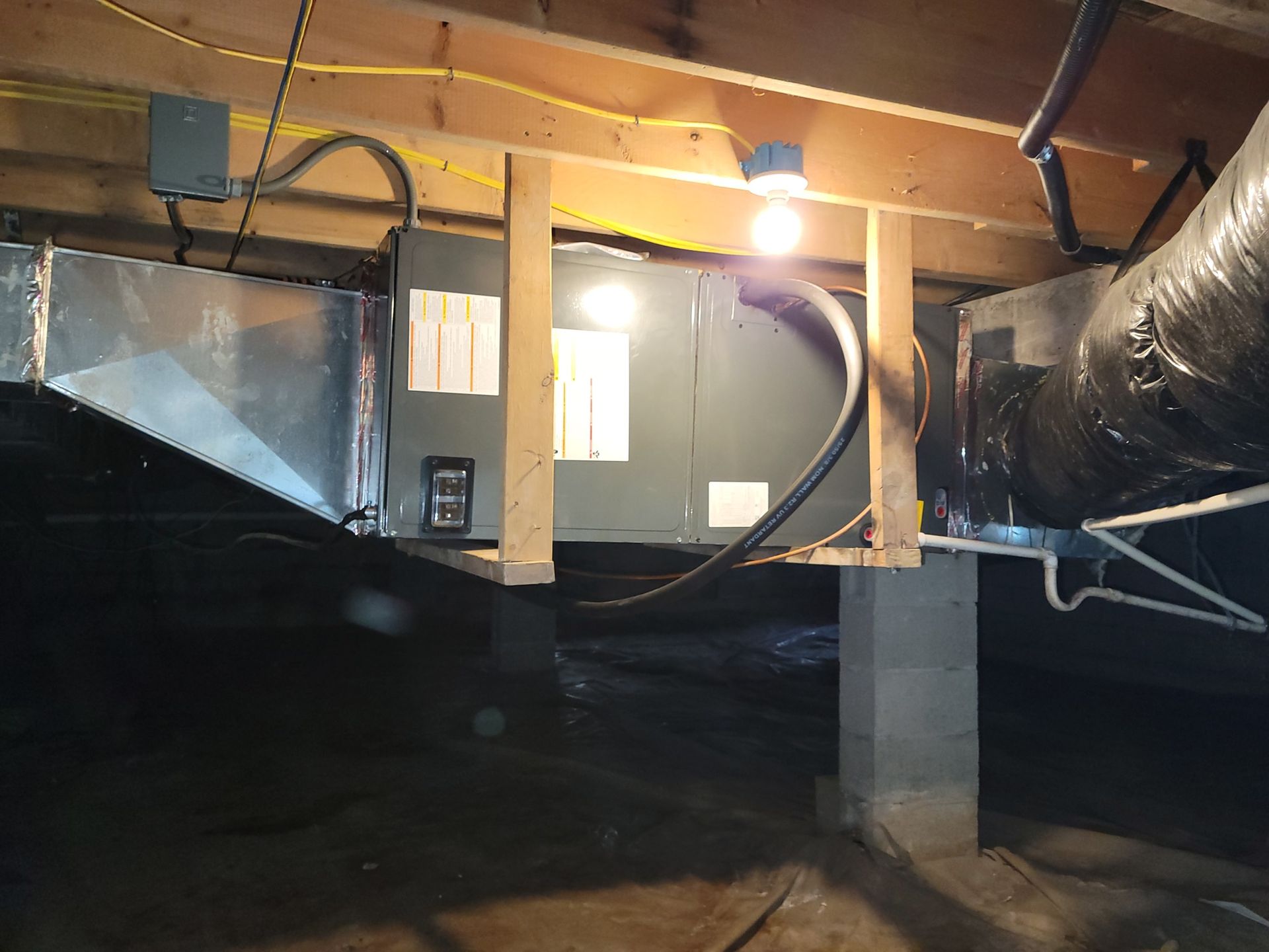 Basement crawlspace with exposed ductwork, insulation, and a lit hanging bulb under wooden joists.