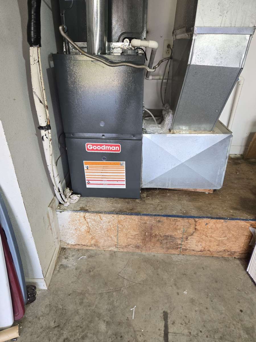 Goodman HVAC unit and ductwork in a basement utility area, beside a concrete step and floor