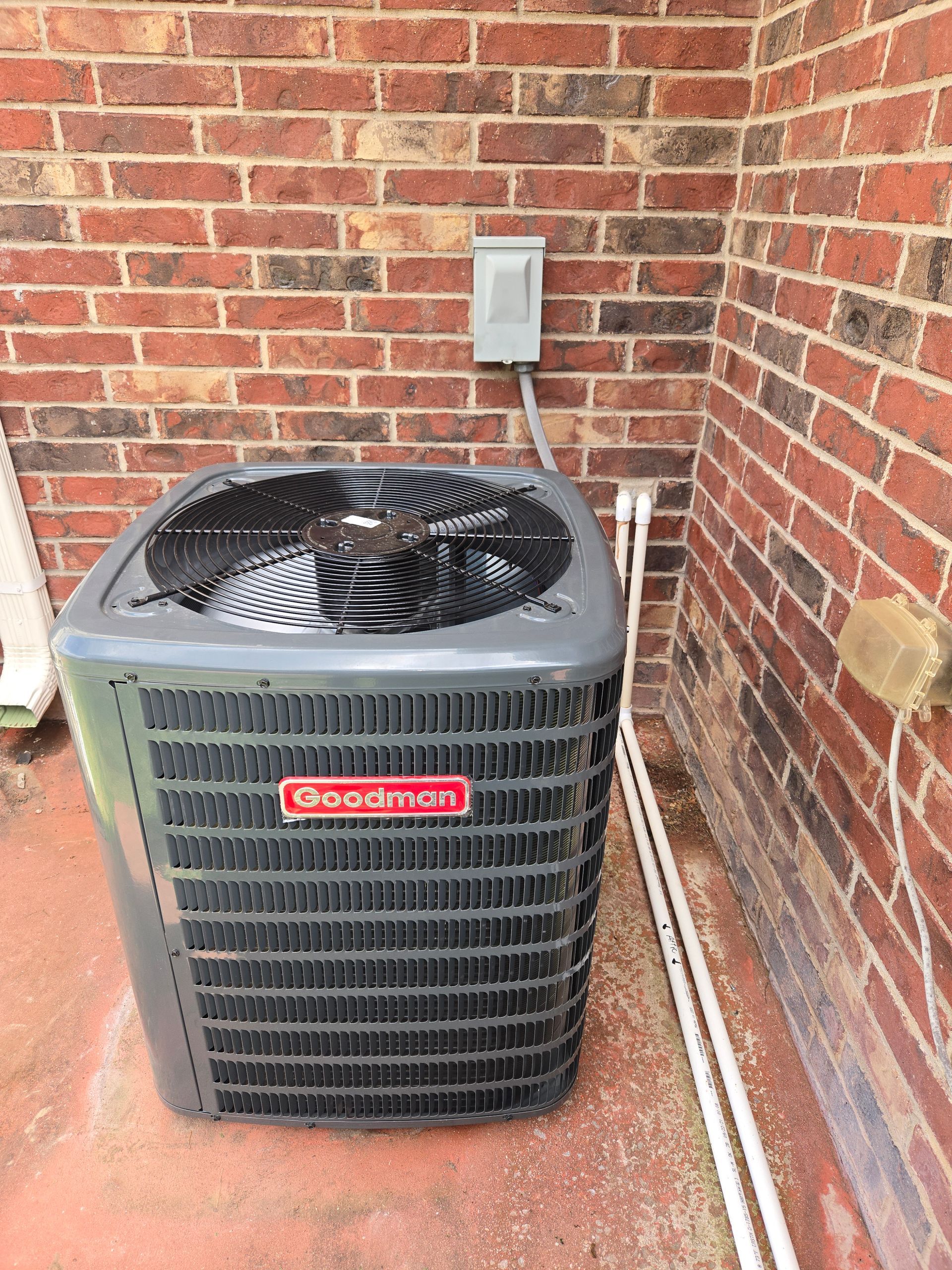 Outdoor HVAC unit beside a brick wall with a fan on top and an electrical box above it