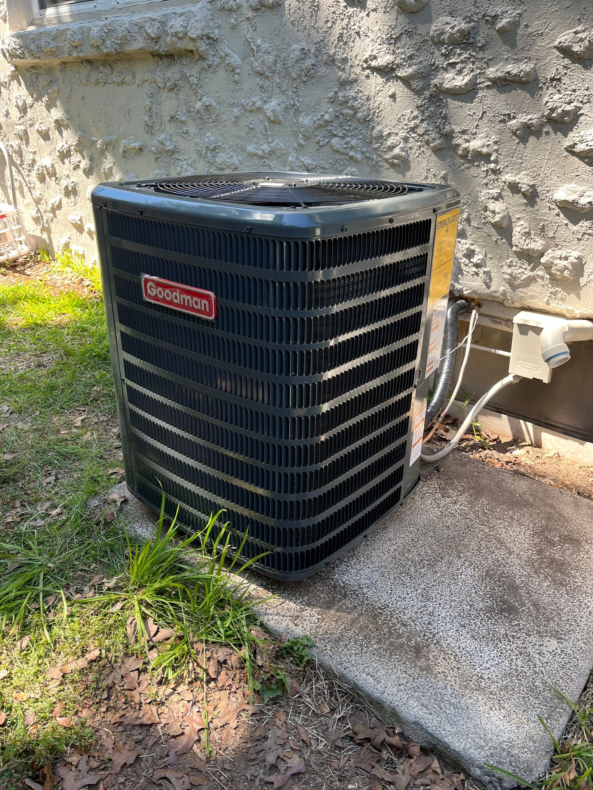 Black Carrier outdoor air conditioner unit beside a stone wall and grass.