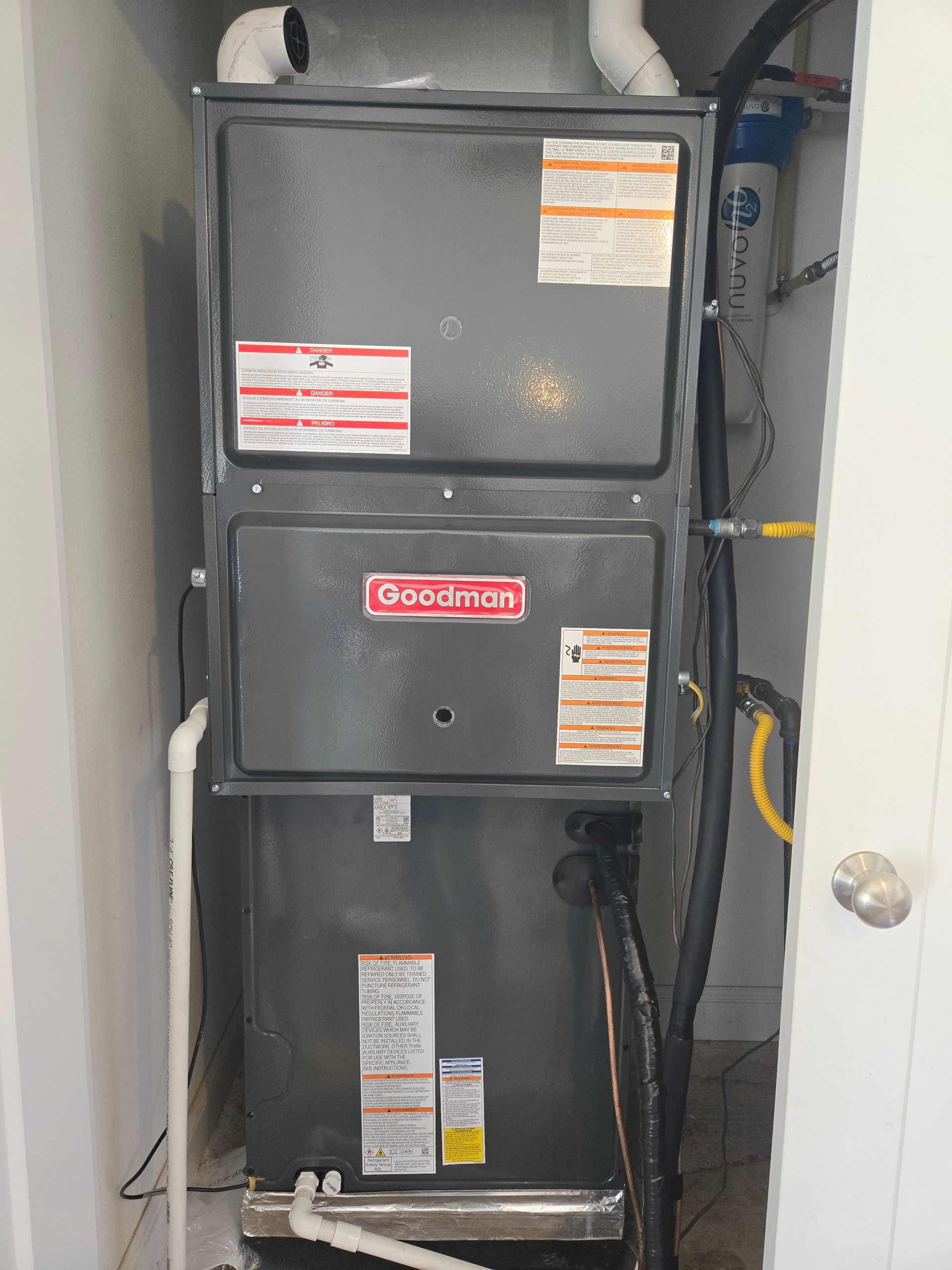 Gray HVAC unit and ductwork in a closet, with labels and wiring visible beside a door.
