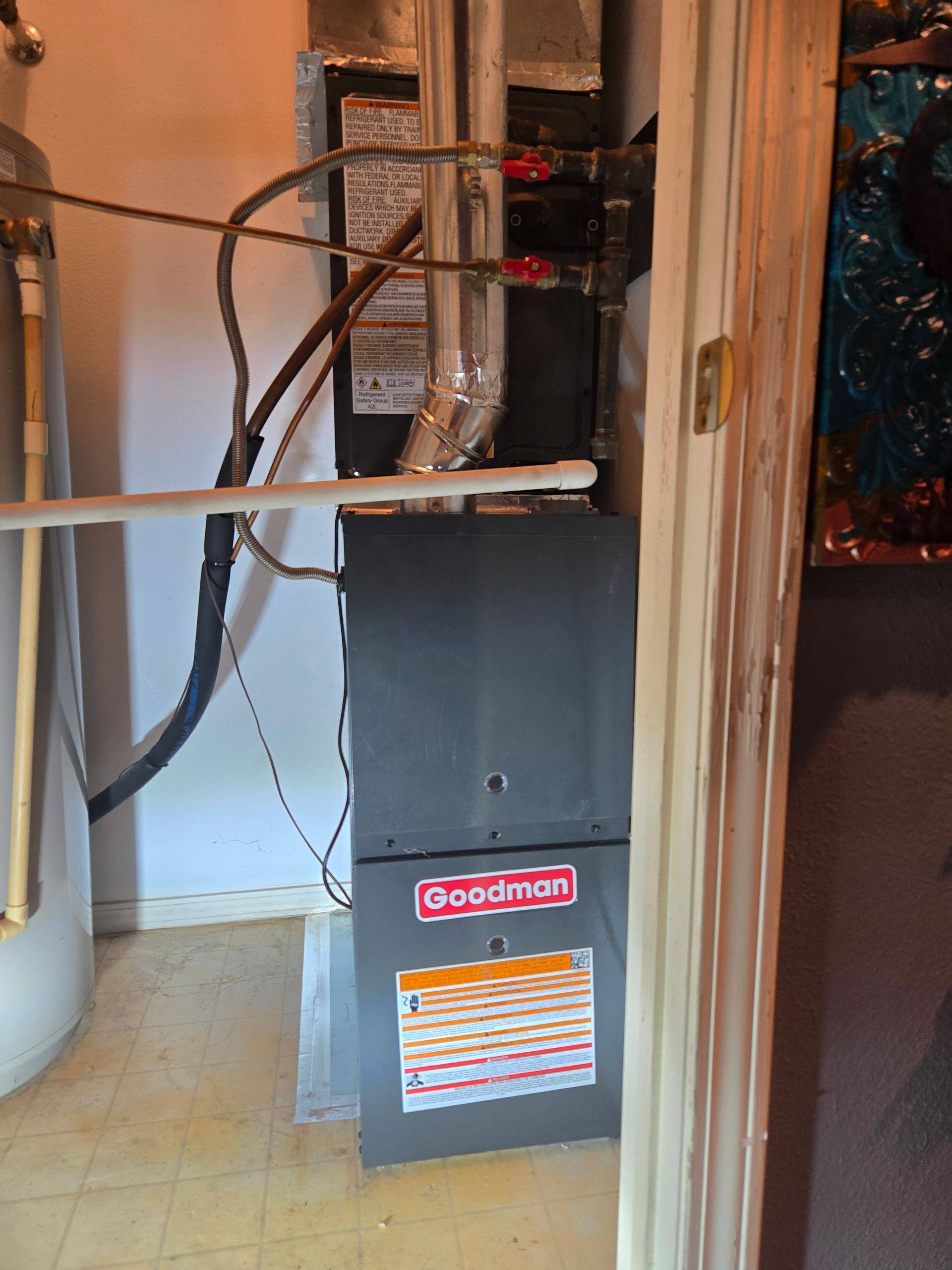 Gray Goodman furnace with ducts and pipes in a utility closet