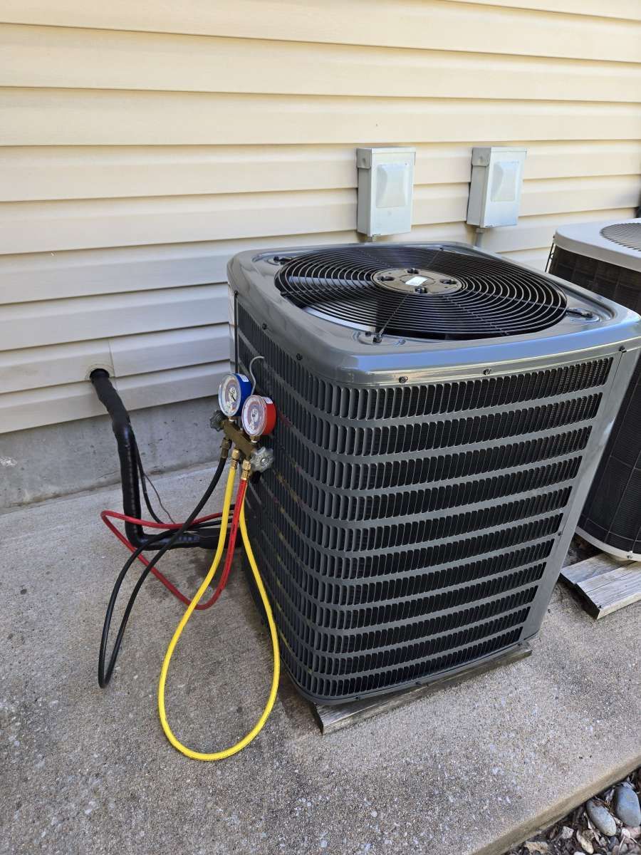 Outdoor air conditioner unit beside beige siding, with service gauges and hoses attached.